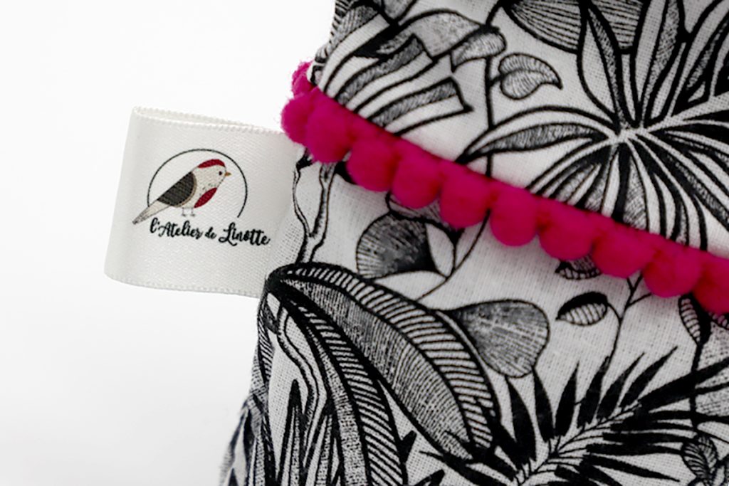 Gros plan sur une étiquette textile tissée avec le logo L'Atelier de Linotte, création d'identité visuelle par Well Com Studio graphique à Albi.