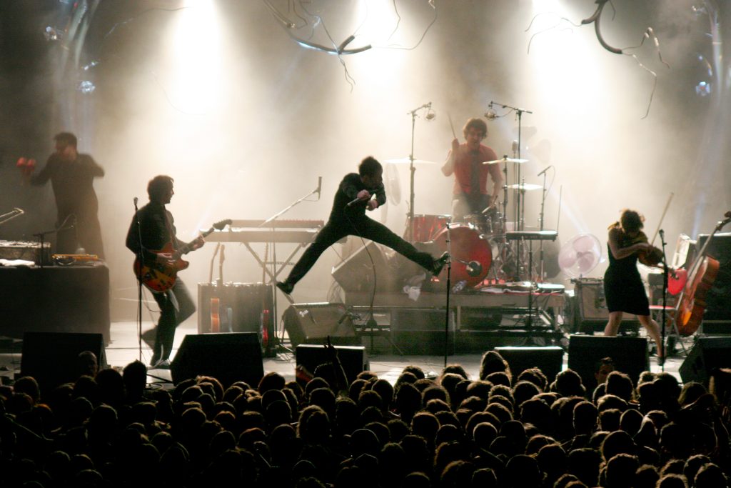 Photographie de concert du groupe Dionysos à Toulouse (événement AFEV) : le chanteur Mathias Malzieu en plein saut sur scène, ambiance rock et énergie live capturée par Well Com Studio Graphique à Albi.