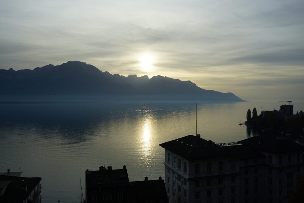 Vue panoramique du Lac Léman au crépuscule avec reflets du soleil sur l'eau et silhouettes de montagnes, photographie d'ambiance et gestion de la lumière par Well Com Studio Graphique à Albi.