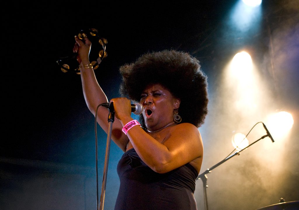 Photographie de concert noir et blanc du groupe The BellRays au Zguen Festival (2009) : la chanteuse Lisa Kekaula chantant avec un tambourin, énergie Rock & Soul capturée par Well Com Studio Graphique à Albi.