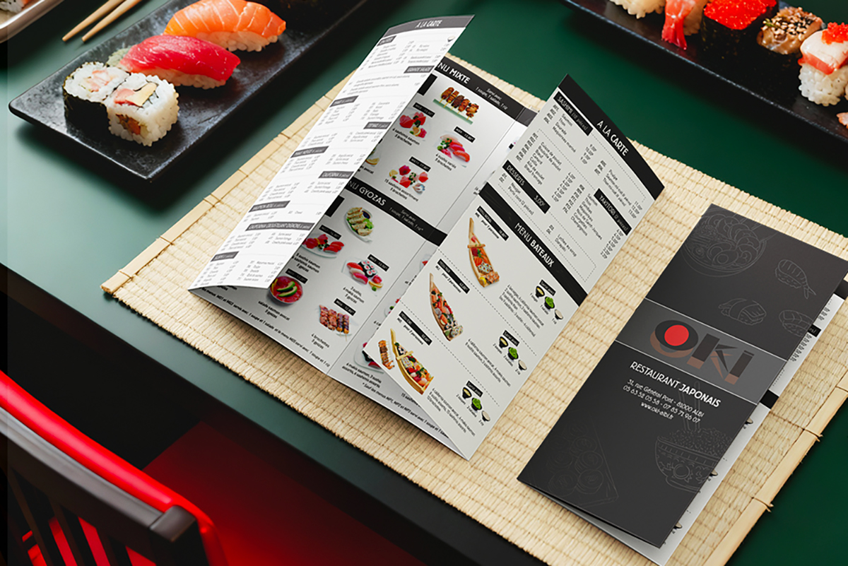 épliant menu 3 volets du restaurant OKI présenté sur une natte en bambou avec des sushis, création graphique de menu restaurant par Well Com Studio Graphique à Albi.
