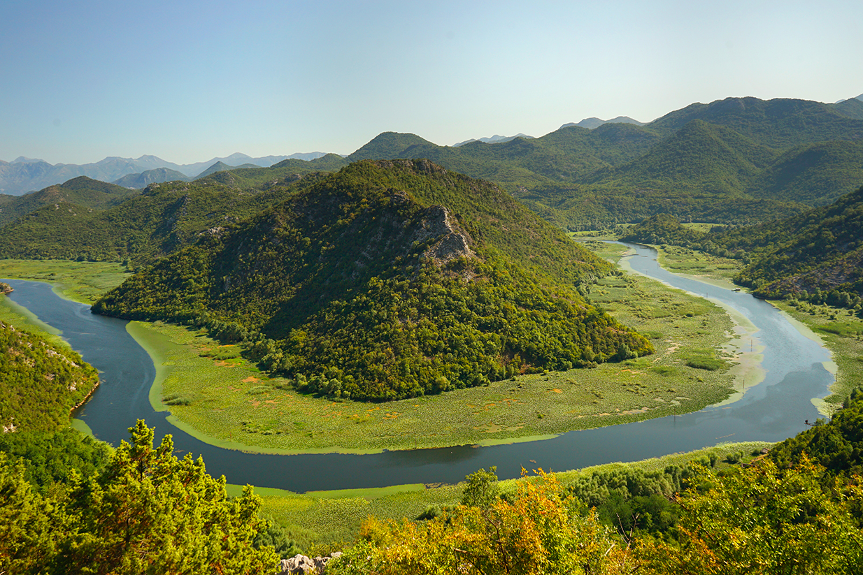 Vue panoramique du méandre de la rivière Crnojević (Lac Skadar) au Monténégro : courbe d'eau en fer à cheval entourée de collines verdoyantes, photographie de paysage nature par Well Com Studio Graphique à Albi.