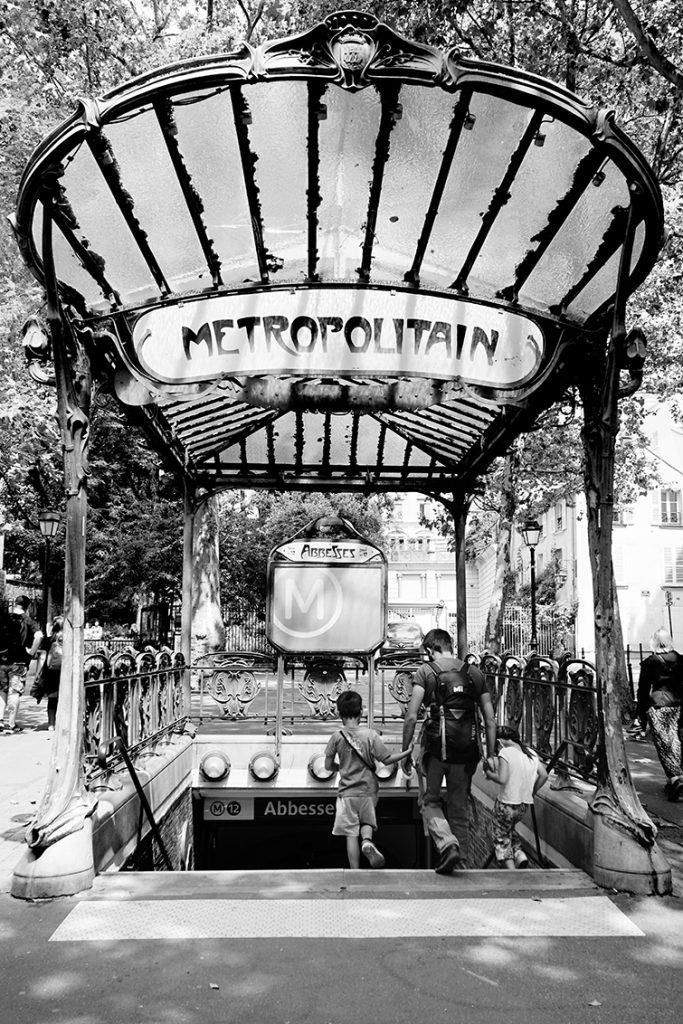 Photographie noir et blanc de l'entrée de métro Art Nouveau station Abbesses à Paris (architecture Hector Guimard), détail de la typographie et de la verrière par Well Com Studio Graphique à Albi.