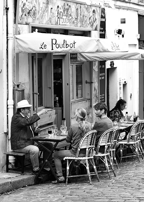 Scène de rue noir et blanc à Montmartre (Paris) : discussion animée à la terrasse du restaurant Le Poulbot, photographie de vie urbaine et lifestyle par Well Com Studio Graphique à Albi.