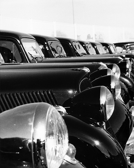 Photographie argentique noir et blanc d'une rangée de voitures anciennes (Citroën Traction) avec focus sur les phares et calandres, jeu de répétition graphique par Well Com Studio Graphique à Albi.