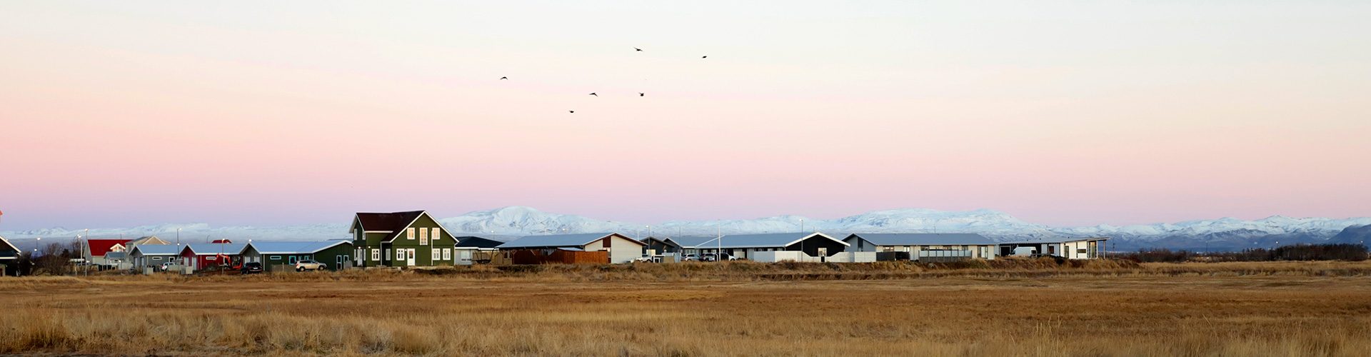Panorama d'un village islandais avec maisons colorées et chaîne de montagnes enneigées sous un ciel pastel, photographie de paysage par Well Com Studio Graphique à Albi.